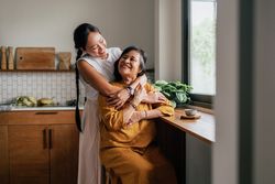 Adult woman hugging mom by kitchen window