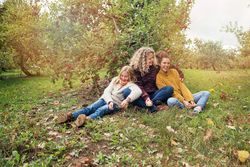 mom and two daughters sitting in orchard under apple tree