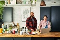 Man in plaid flannel with young woman in overalls cooking in kitchen