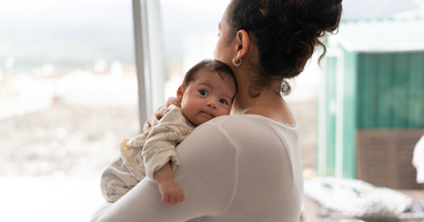 Mom holding a newborn on her shoulder while looking out a window