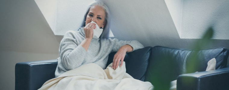 Woman sitting on the coach and blowing her nose from being sick