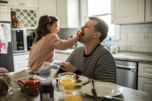 Girl in pink sweater sitting on kitchen table feeding her father strawberries