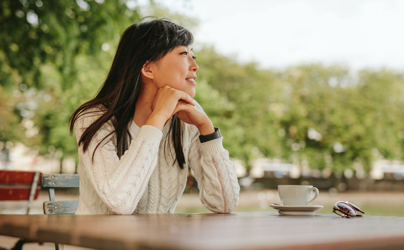 Woman in sweater looking into distance at cafe table