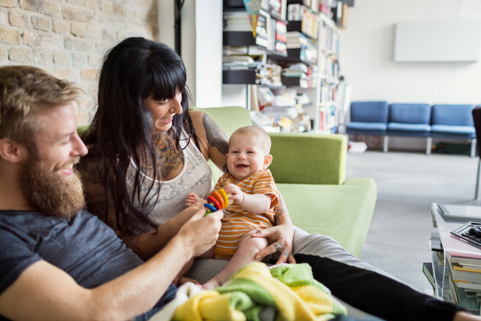 Young mother and father at home on couch holding baby