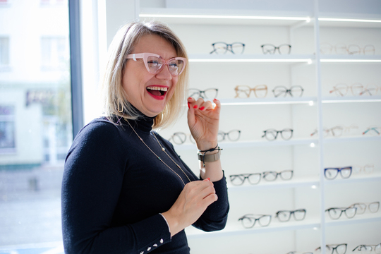 A senior woman trying on pink glasses at eye doctor