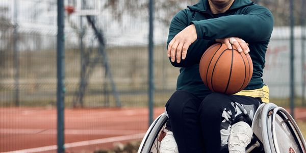 older man in wheelchair playing basketball outside