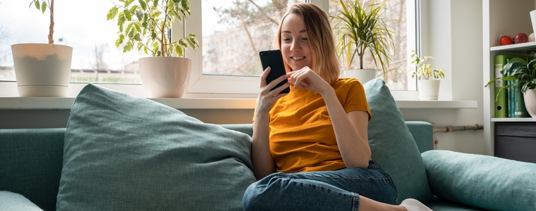 Woman sitting on a couch with a cat, using a smart phone