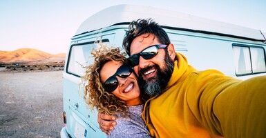 Couple in sunglasses taking road trip selfie in front of van