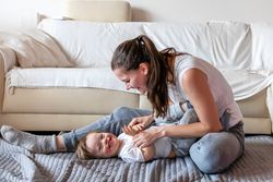 a mom playing with her smiling baby on a blanket on the floor