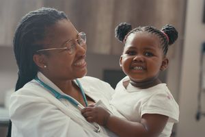 a smiling doctor holding a smiling young patient in an exam room.