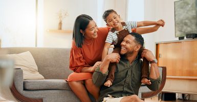 Mom and dad smiling at eachother with toddler on dad's shoulders