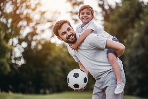 dad with child on his back holding soccer ball