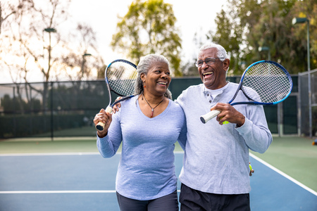Smiling senior couple with racquets on a tennis court.
