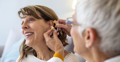 a smiling woman having a hearing aid fitted.