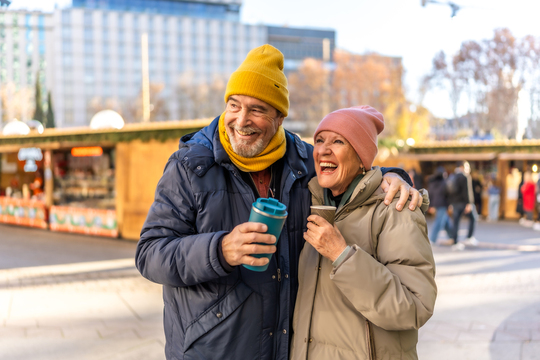 older couple hugging and holding coffees outside in winter