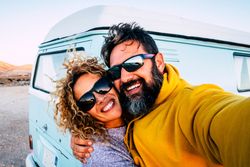 Couple in sunglasses taking road trip selfie in front of van