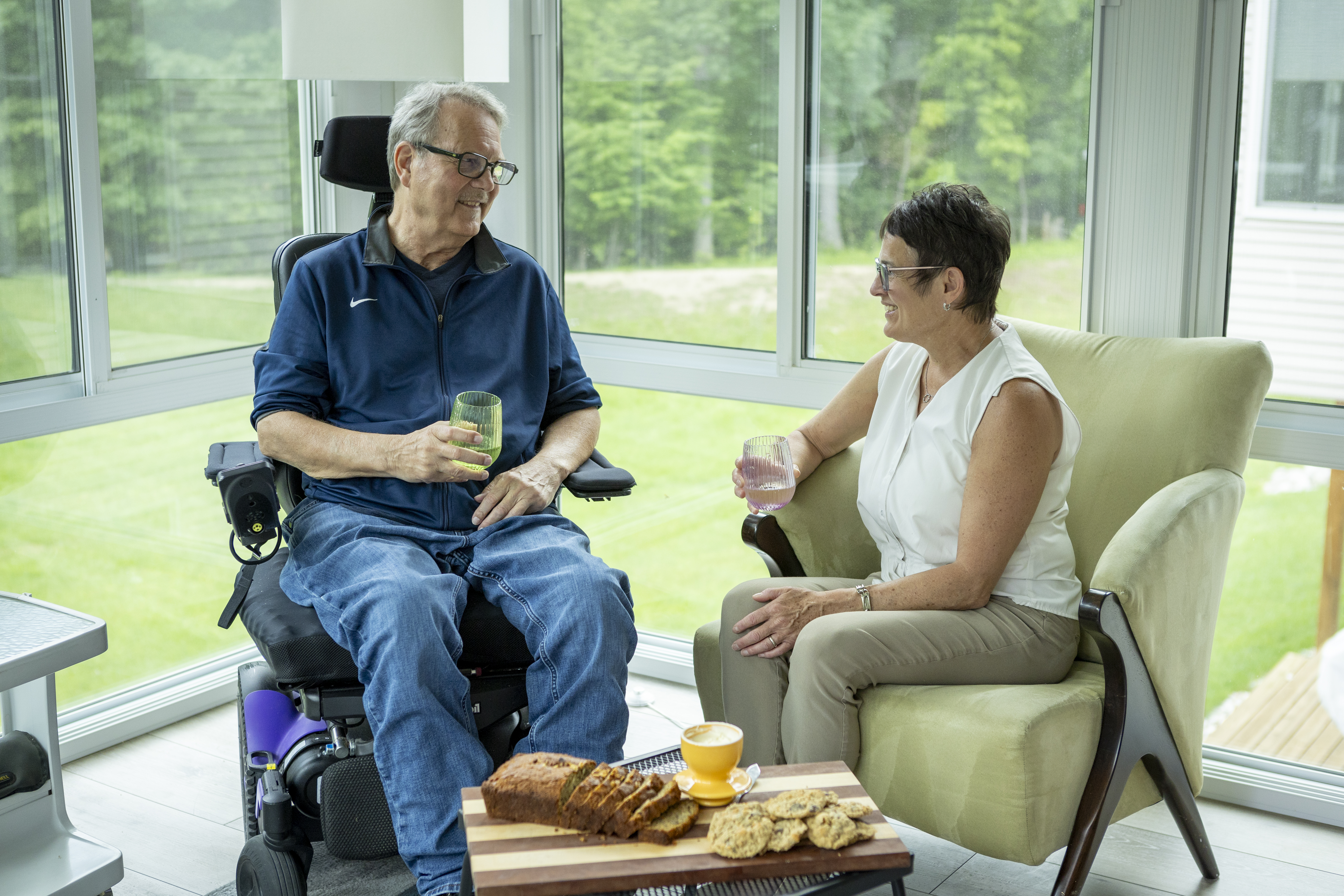 Older man and his wife sitting in their sunroom enjoying a glass of water and snacks