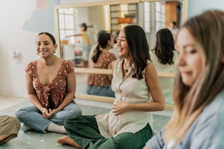 smiling women sitting in a circle one with hand on belly