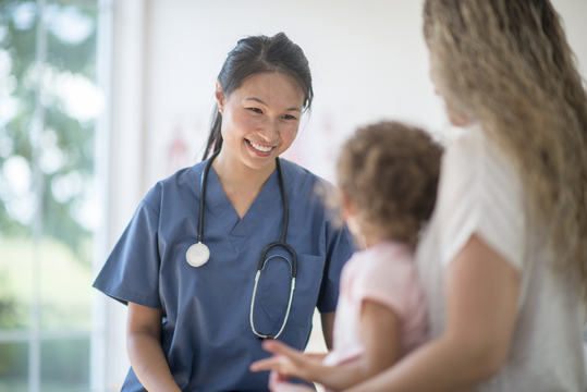 Female doctor smiling at toddler and her mom