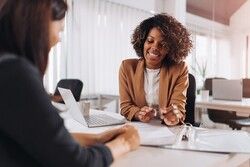 woman at desk helping another with paperwork