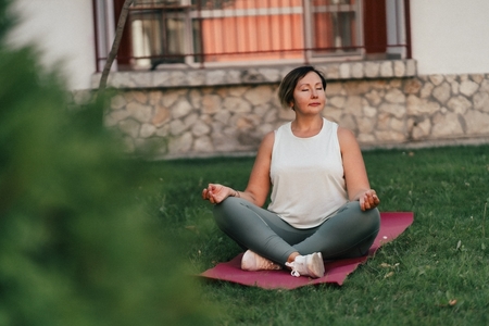 a middle-aged woman practices yoga on her front lawn