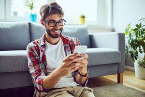 man in glasses sitting on living room floor looking at smartphone