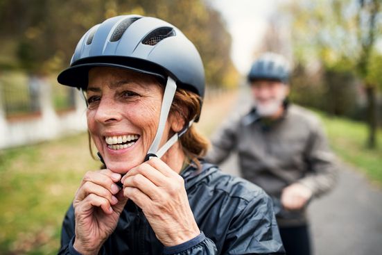 senior woman in bike helmet on trail outdoors with man in background