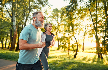 older couple briskly jogging with sun shining through trees