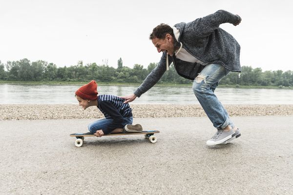 Smiling dad pushing his son on a skateboard 