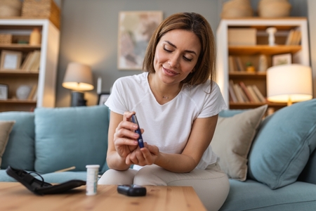 younger woman checks blood sugar at home on her couch