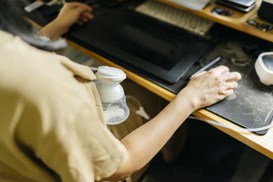 woman using a breast pump and working sitting at a computer