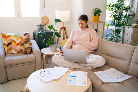 Pregnant mom on the couch taking notes with laptop