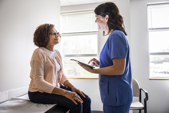 Provider in scrubs reviewing treatment plan on tablet with female patient in clinic