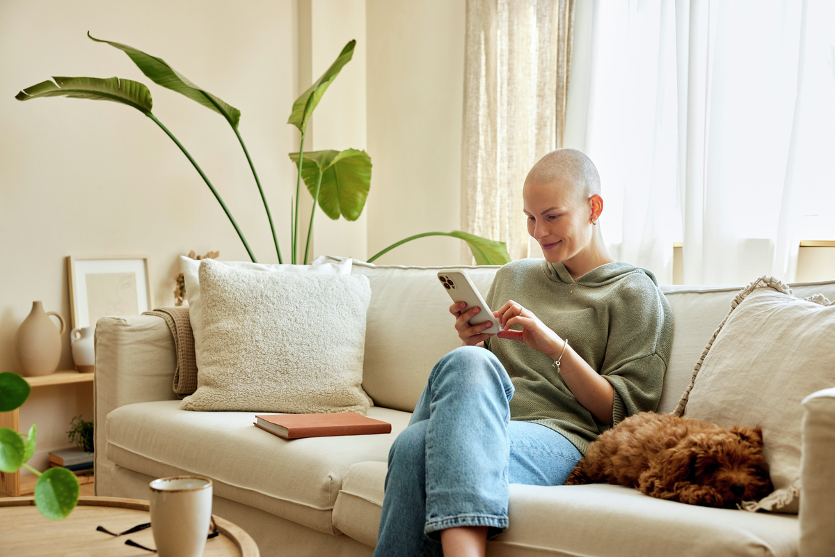 A younger female cancer patient receives support from her living room on her mobile phone