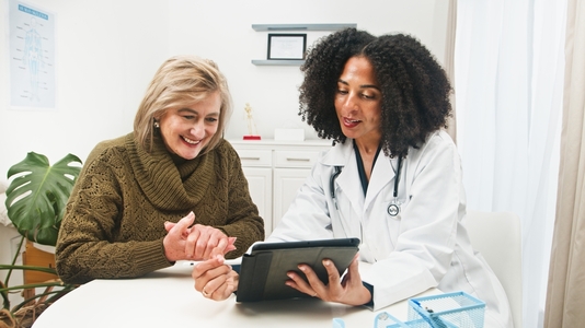 An older woman reviews health results on a tablet with her younger female doctor in her office