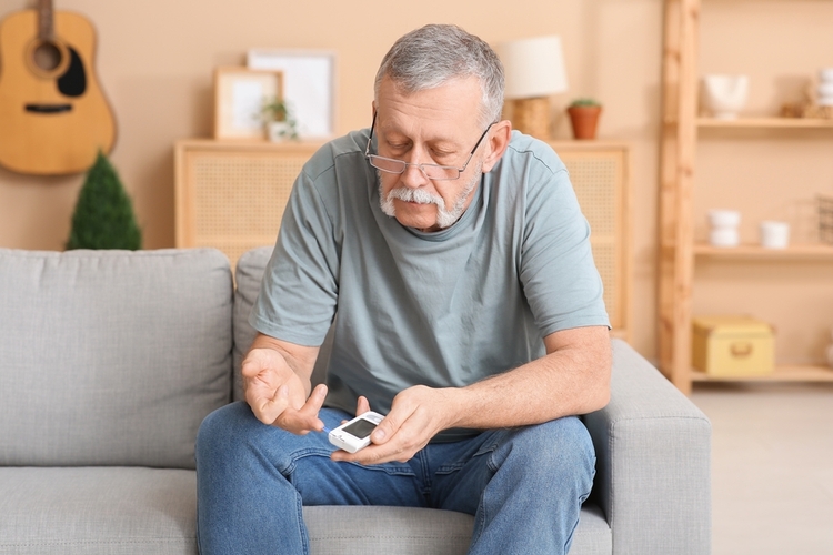 An older man in a t-shirt with an awesome handlebar mustache checks his blood glucose in his living room