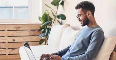 young man sitting on couch working on laptop