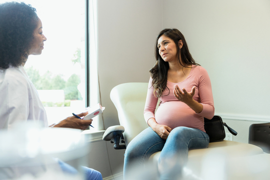 a pregnant woman sitting in a dentist chair talking to doctor or dentist