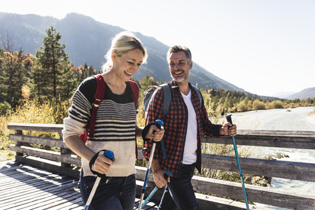 couple walking with poles on nature trail bridge