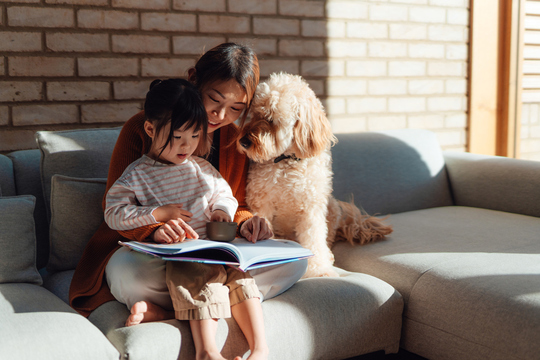 mother and daughter reading together on couch with dog
