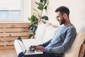 young man sitting on couch working on laptop