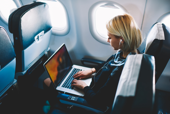 Woman wearing headphones and working on laptop on airplane