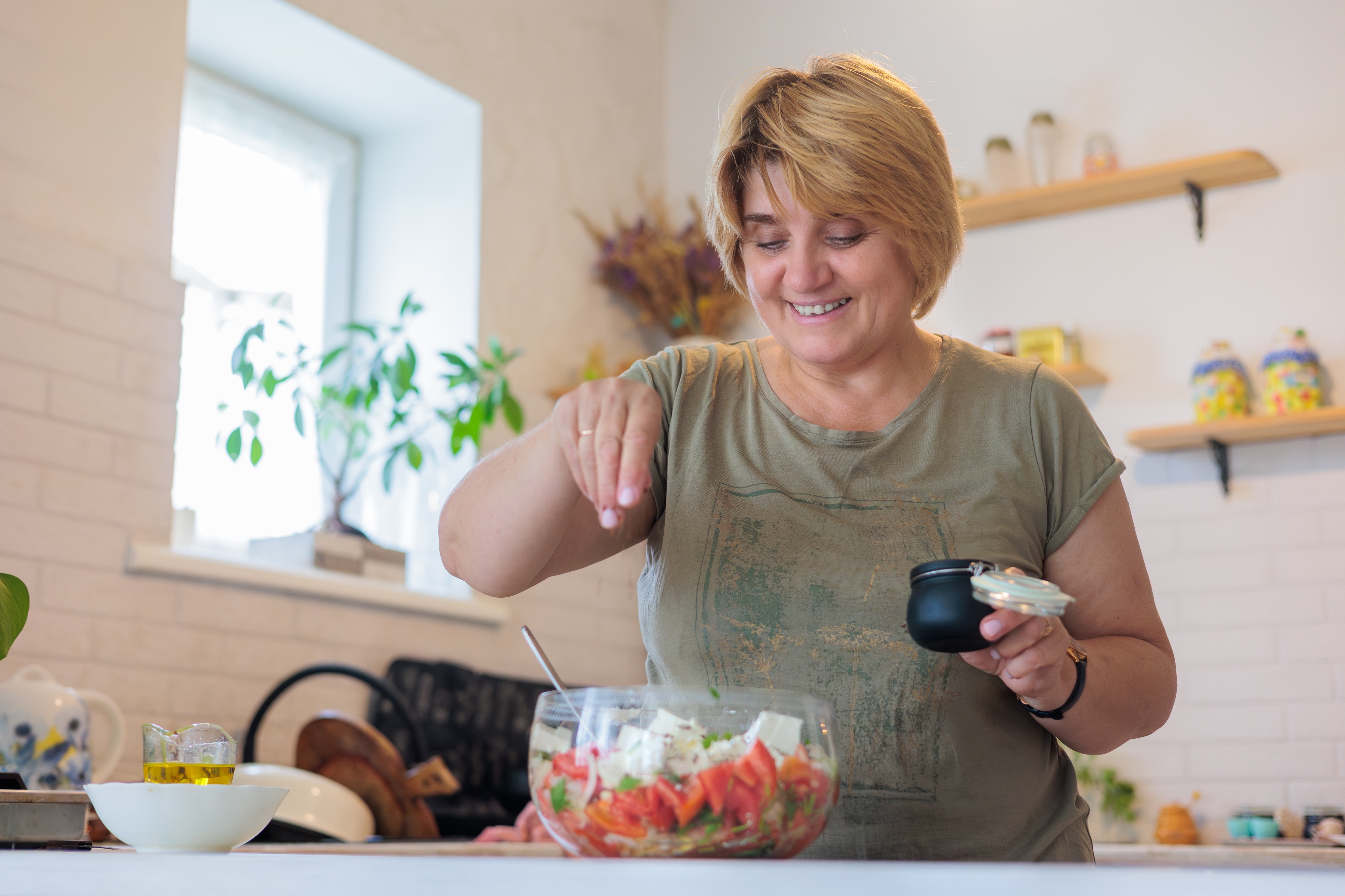 A middle aged woman prepares a healthy salad in her modern kitchen
