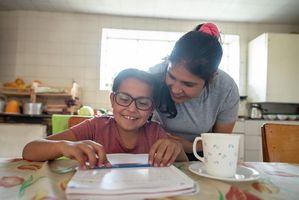 Mother helping daughter with schoolwork at breakfast table