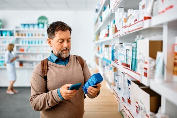 man in pharmacy looking at product and phone