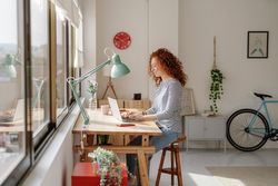 Young woman with curly hair working on her laptop in a modern apartment 