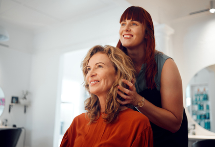 young female hairdresser styling smiling woman's hair in salon