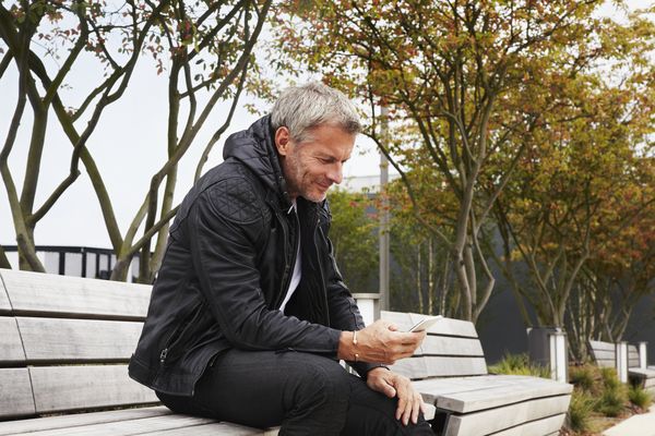 man reading smartphone on park bench