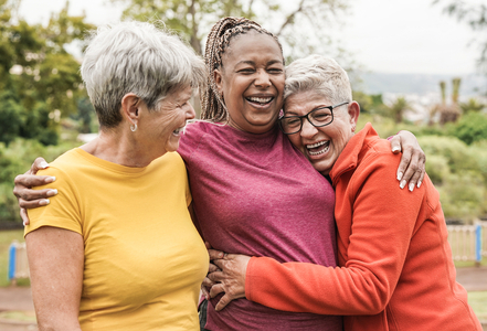 three laughing senior woman friends hugging outdoors