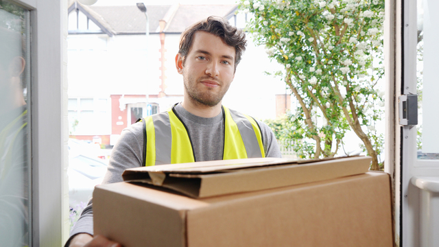 delivery man in high visibility vest holding packages in doorway